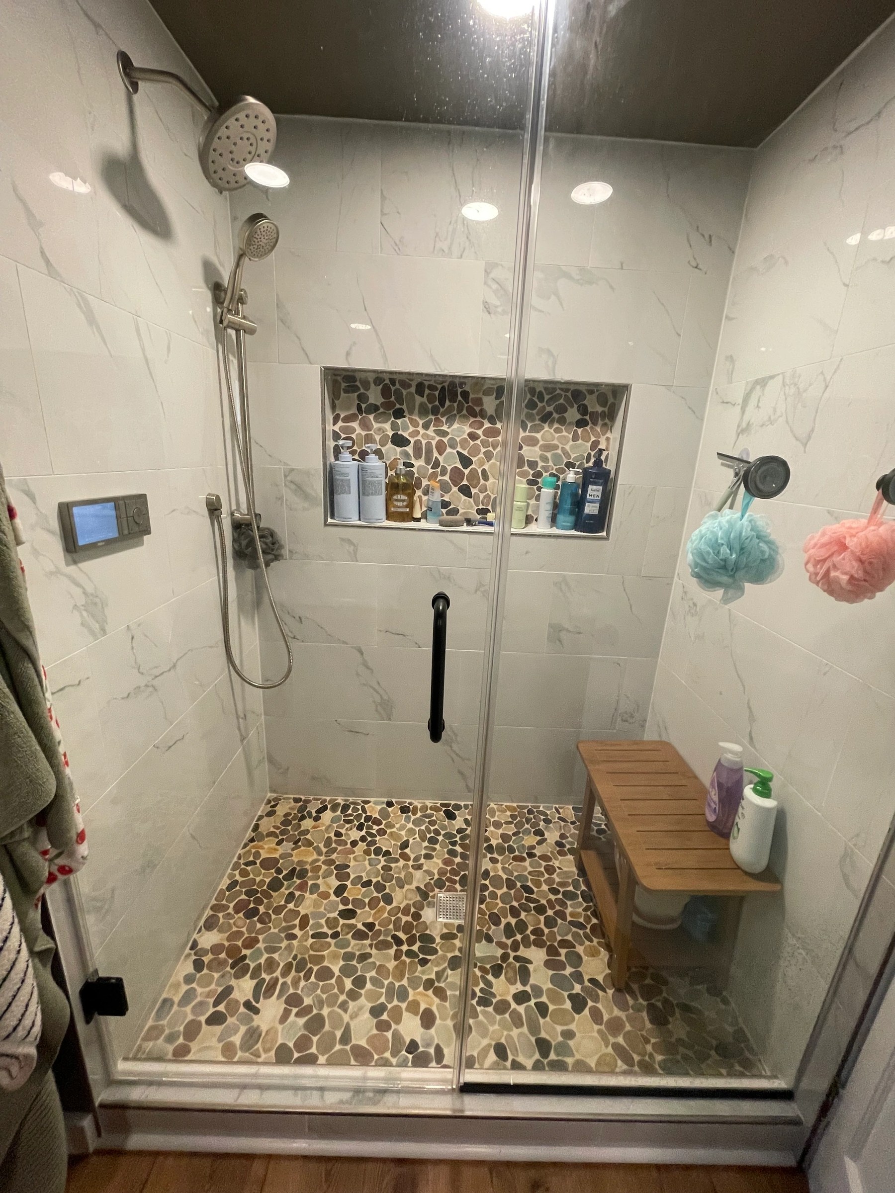 Custom tiled walk-in shower with marble-look walls, a pebble floor, recessed niche and a digital shower control