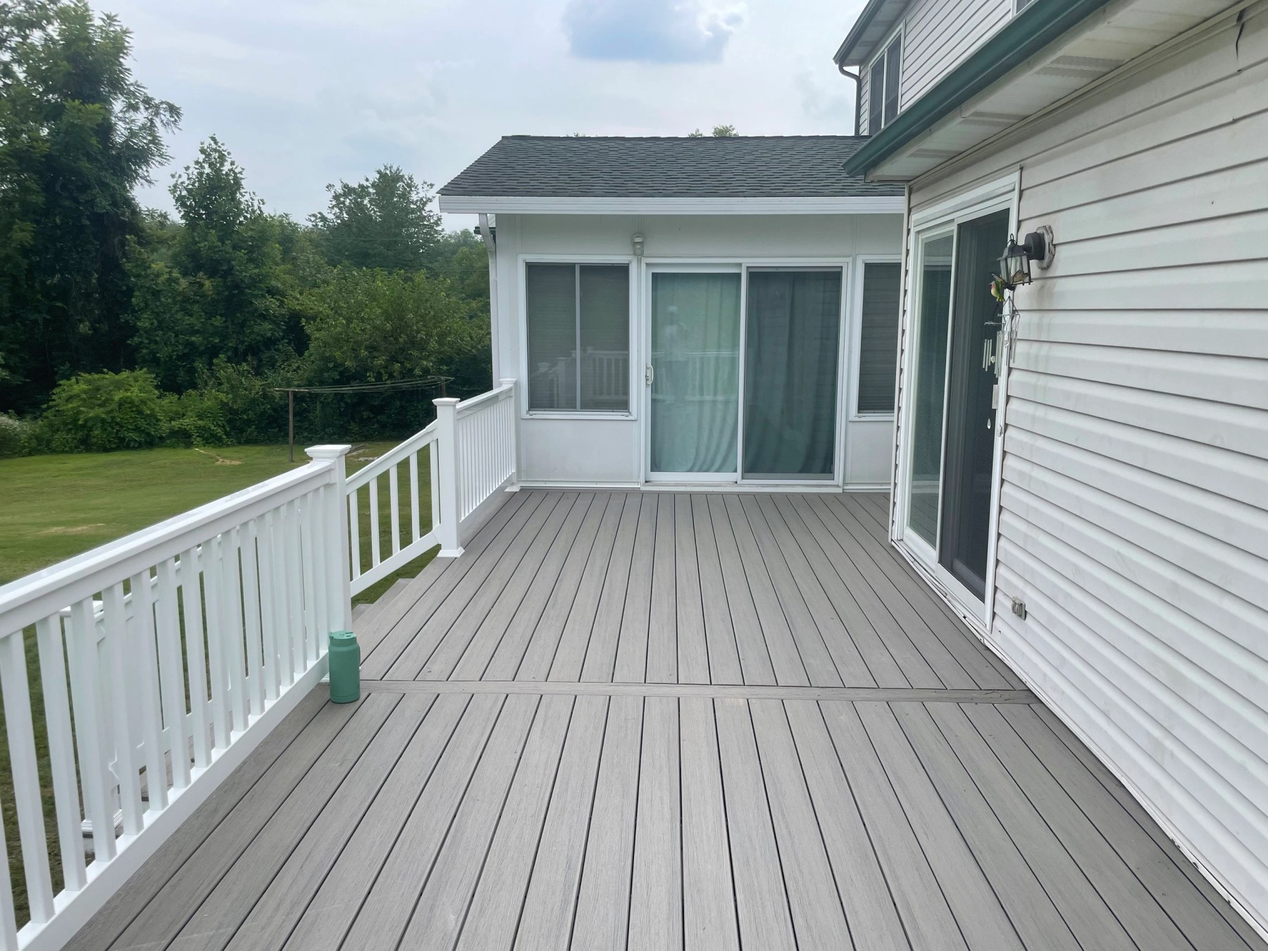 Composite deck with grey boards and a white vinyl railing running alongside a sunroom