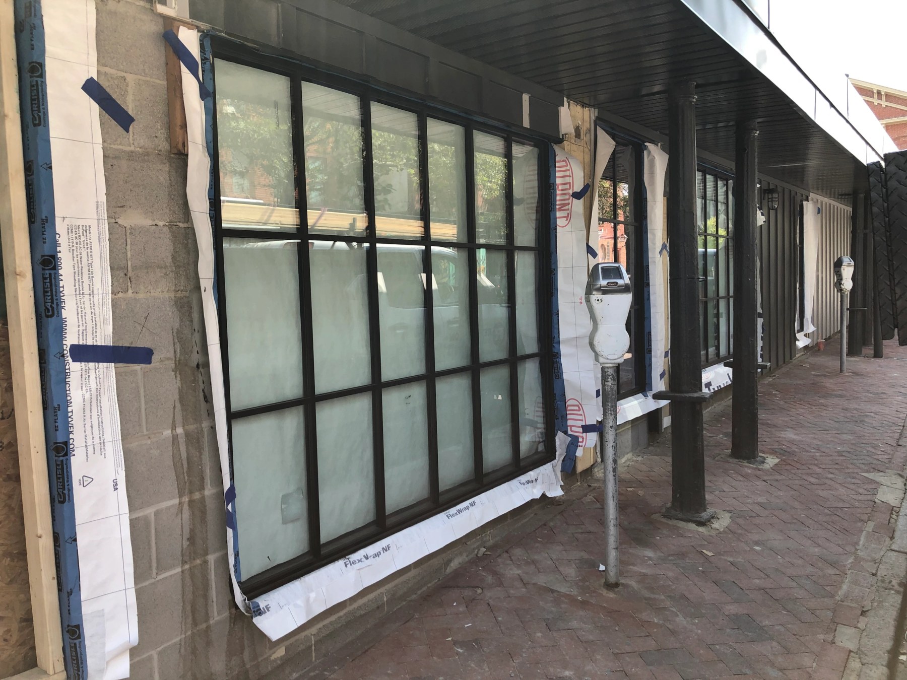 Large black-framed commercial storefront window set into a masonry wall with flashing tape around the opening